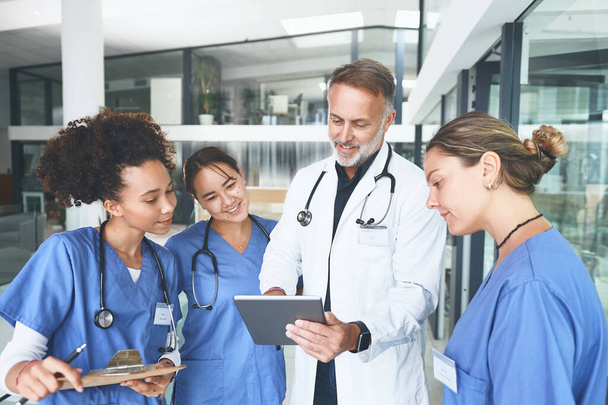 This new medication is changing everything. a handsome mature doctor standing with his nurses and using a digital tablet during a discussion - Zdjęcie, obraz