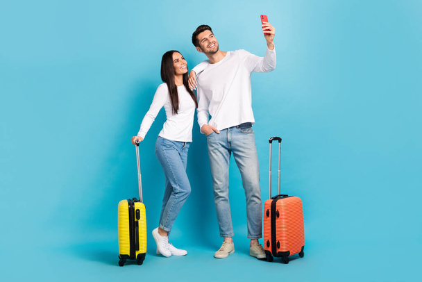 Photo of two positive cheerful glad couple people wear white shirts doing selfie prepared to travel isolated on blue color background. - Foto, Imagen