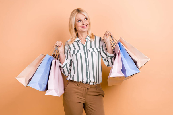 Photo of pleasant senior woman bob hairstyle wear striped shirt holds shopping bags look empty space isolated on pastel color background. - Fotografie, Obrázek