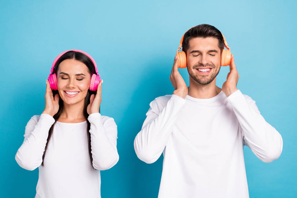 Photo of two peaceful cheerful people closed eyes beaming smile arms touch headphones isolated on blue color background. - Photo, Image