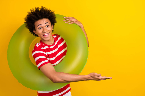 Photo of handsome guy hold inflatable ring arm demonstrate empty space isolated on yellow color background. - Fotoğraf, Görsel