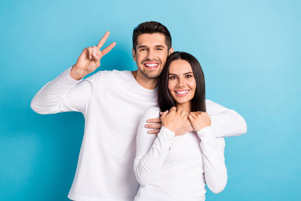 Photo portrait of nice young guy girl hugging show v-sign toothy smile posing wear trendy white clothes isolated on blue color background. - Foto, Imagen