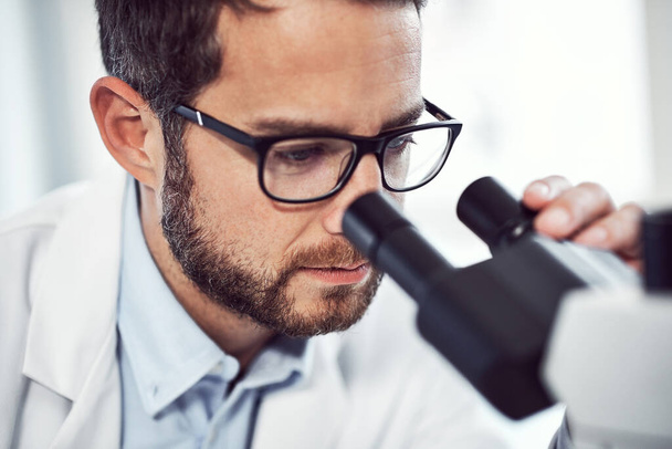 It says interesting every time I do this. a focused young male scientist looking through a microscope while being seated inside of a laboratory - Foto, Imagen