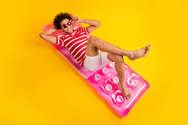 Full length photo of funky adorable guy dressed red t-shirt sunbathing air bed isolated yellow color background. - Fotó, kép