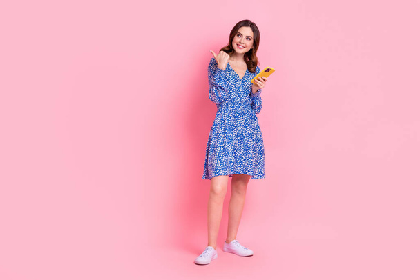 Full length photo of lovely lady wear trendy clothes thumb direct look empty space modern device shop isolated on pink color background. - Foto, immagini