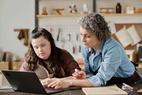 Столяр осматривает новый онлайн-проект на ноутбуке вместе с девочкой с синдромом пуха в мастерской - Фото, изображение