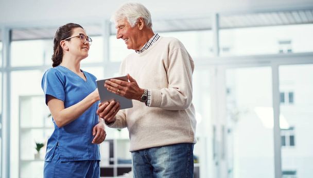 Je hebt me goed geholpen. een jonge vrouwelijke verpleegster en haar oudere patiënt kijken naar een tablet in het bejaardentehuis - Foto, afbeelding