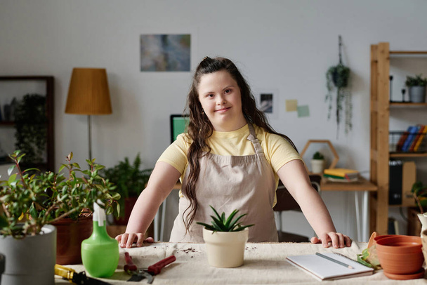 Portrait of girl with down syndrome smiling at camera while planting plants in pots - Photo, Image