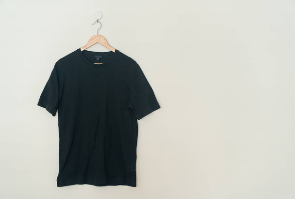 black t-shirt hanging with wood hanger on wall - Photo, Image