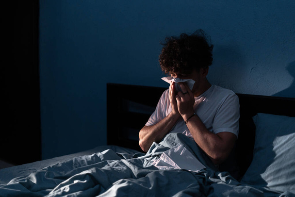 Beau jeune homme souffrant de rhume et la grippe essayant de dormir la nuit, gars éternuant dans un mouchoir dans la chambre. Maladie rhume ou grippe. Concept d'allergie ou de problème de santé. Espace de copie - Photo, image