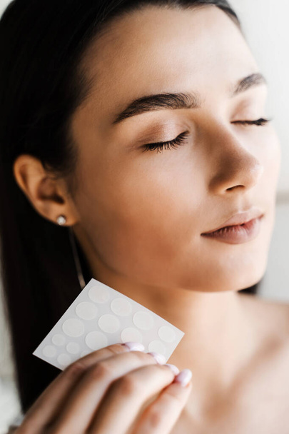 Girl with acne stick round acne patch in hands. Using acne patches for treatment of pimple and rosacea close-up. Facial rejuvenation cleansing cosmetology - Photo, image