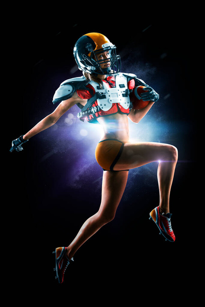 Portrait of attractive brunette female american football player in uniform and jersey T-shirt posing with helmet isolated on the black background - Foto, Imagen
