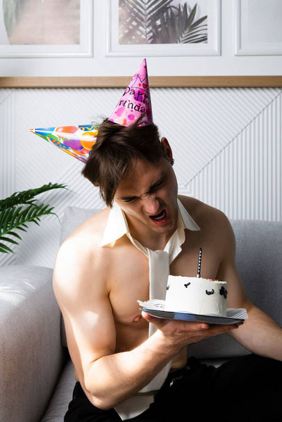 Чоловік без сорочки з краваткою святкує свій день народження, тримає смішний прикрашений торт
 - Фото, зображення