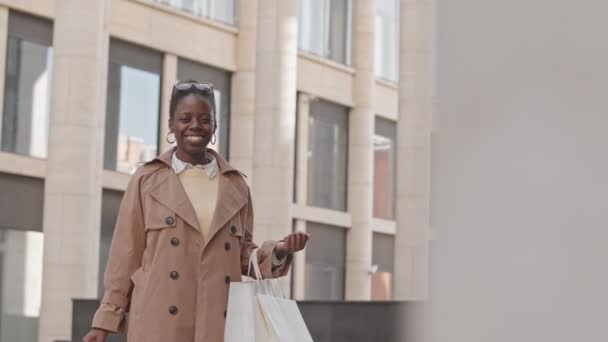 Inclinado retrato slow mo de la joven afroamericana encantada con bolsas de papel posando para la cámara al aire libre - Imágenes, Vídeo