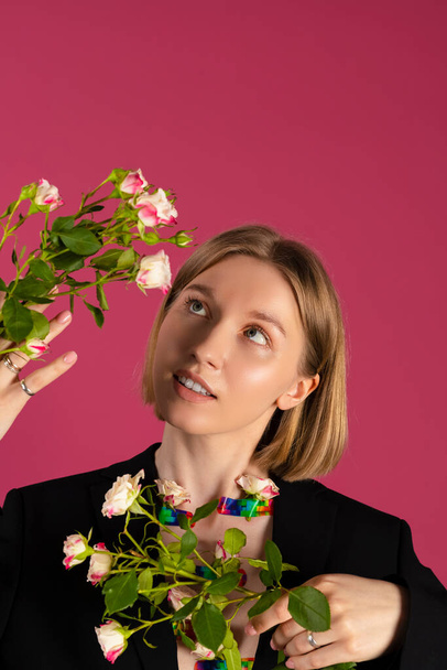 Portrait of a Beautiful tender young blonde hair girl with the Flowers are growing out of the sleeves of her black blazer. isolated on pink background. - Valokuva, kuva
