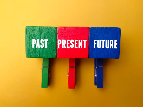 Farbige Holzklammern und Holzwürfel mit dem Wort PAST PRESENT FUTURE auf gelbem Hintergrund - Foto, Bild