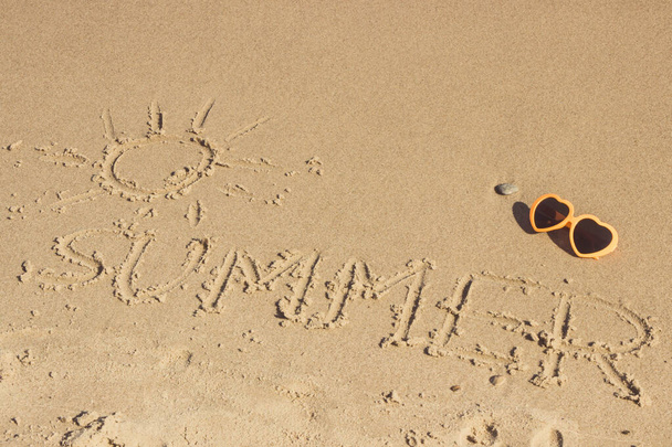 Inscription summer with shape of sun and sunglasses on sand at beach. Concept of vacation time - Foto, imagen