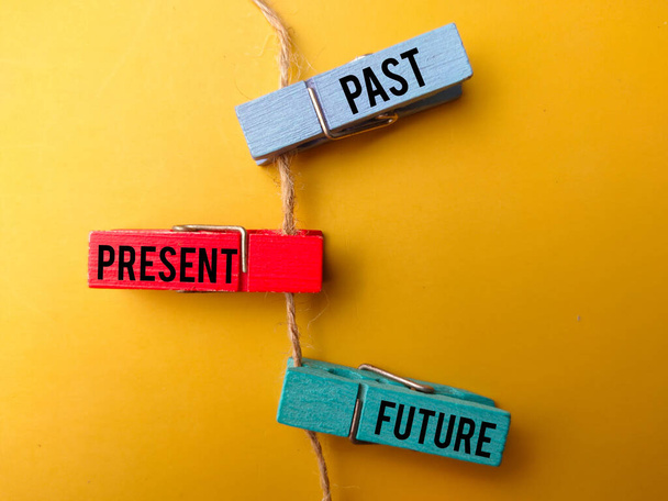 Colored wooden clips and roots with the word PAST PRESENT FUTURE on yellow background - Zdjęcie, obraz