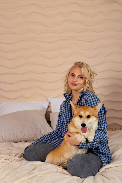 Attractive blonde hair girl and a Welsh corgi Pembroke dog are lying on the bed together. - Foto, Imagem