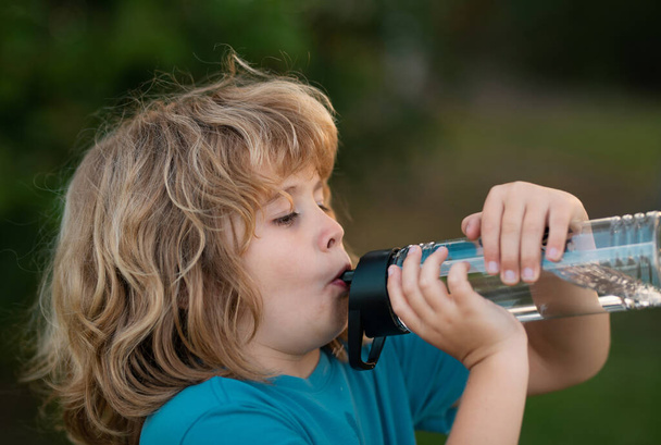 Kid drinking water outdoor. Close up portrait of boy drink water from bottle in the garden - Fotó, kép