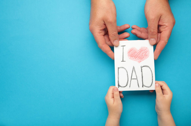 Father's Day. Child hands gives father's day greeting card to her father on blue background. Top view - Фото, изображение