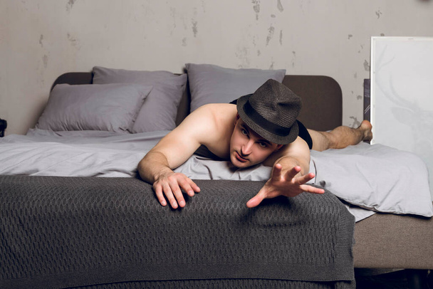 Handsome shirtless slim young man lying on the bed and reaching hand towards the camera. - Фото, зображення