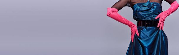 Προβολή μοντέρνας νεαρής γυναίκας με φόρεμα κοκτέιλ και ροζ γάντια που αγγίζουν το ισχίο και ποζάρουν απομονωμένη σε γκρι, μοντέρνα γενιά z fashion concept, λεπτομέρειες, ζώνη, θηλυκό, banner  - Φωτογραφία, εικόνα