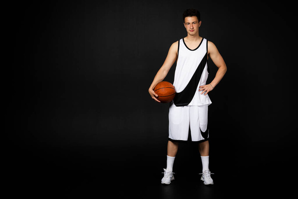 Minsk, Bělorusko - 22. května 2023 - Pohledný mladý basketbalista v bílém sportovním oblečení v akci s míčem v plné délce. Izolováno na černém pozadí. - Fotografie, Obrázek