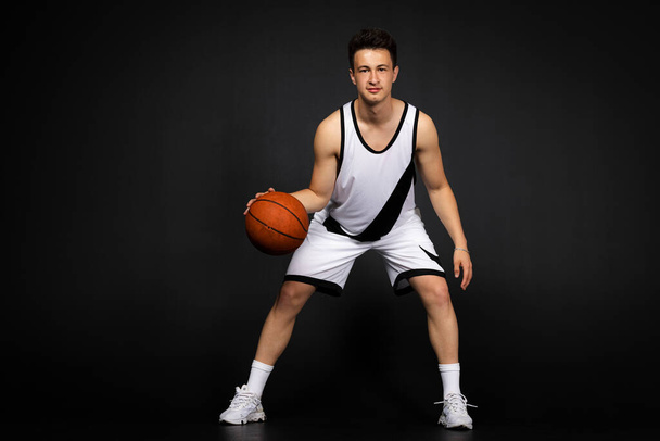 Minsk, Bielorussia - 22 maggio 2023 - Bellissimo giovane giocatore di basket in abbigliamento sportivo bianco in azione con la palla, a tutta lunghezza. Isolato su sfondo nero. - Foto, immagini