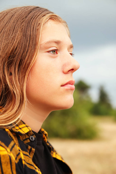Sad serious girl. Portrait preteen girl on the gray sky background. Girl 15 years old. Blonde long hair. Outside. Attractive teenager. Teen girl. Blurred. Closeup. Out of focus. - Photo, Image
