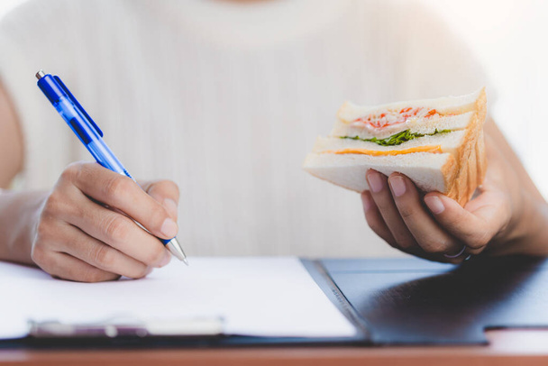 Hand holding a delicious sandwich and taking note for eating while working concept. - Фото, изображение