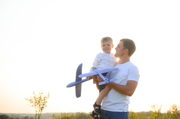 Szczęśliwy ojcowski moment. Ojciec bawi się z synem o zachodzie słońca zabawką w samolocie. - Zdjęcie, obraz