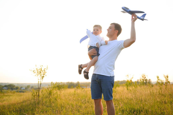 Happy father child moment. Father piggybacking his boy at sunset while he's playing with toy plane - Zdjęcie, obraz