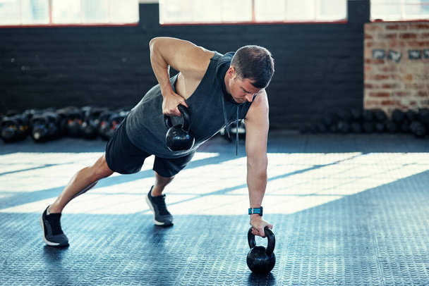 Sore, the most satisfying pain. a young man doing push ups with kettlebells in a gym - Foto, Bild