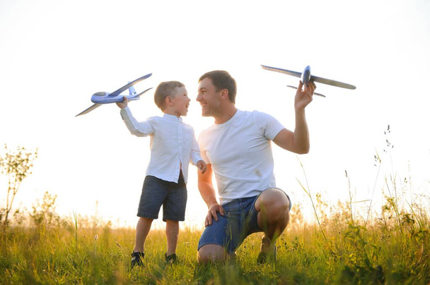 Cute little boy and his handsome young dad are smiling while playing with a toy airplane in the park - Foto, Imagen