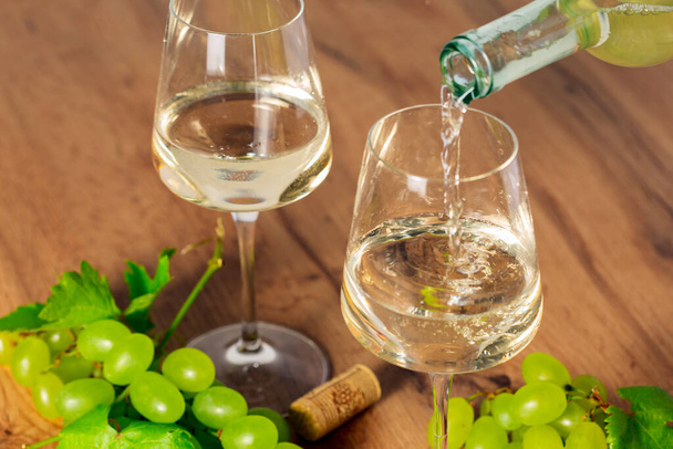 наливать белое вино в бокал с осенним виноградом, старым деревянным фоном, избирательным фокусом - Фото, изображение