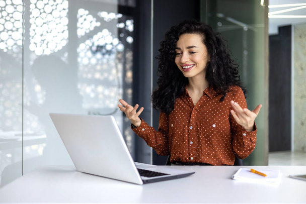 Happy hispanic businesswoman working in modern office using laptop for video call and online meeting with fellow employees, woman smiling and having fun giving a presentation. - Foto, imagen