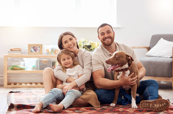 Mom, dad and portrait of kid with dog in living room for quality time, love and care together at home. Mother, father and happy family with child, pet pitbull and relax for happiness on carpet floor. - Foto, Bild