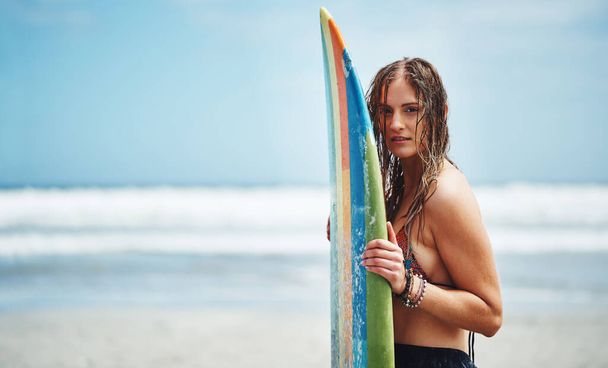 時間を把握し、いくつかの波をリッピングする。サーフボードを持つビーチに立つ魅力的な若い女性の肖像画 - 写真・画像