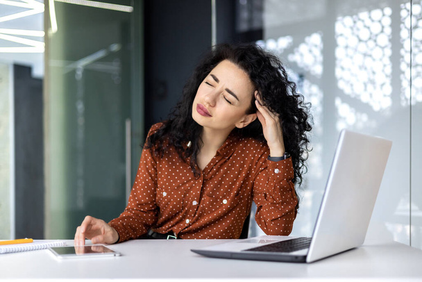 Overtired hispanic business woman working inside modern office, office worker with laptop having severe headache. - Photo, Image