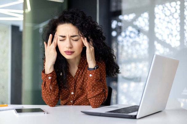 Overtired hispanic business woman working inside modern office, office worker with laptop having severe headache - Photo, image