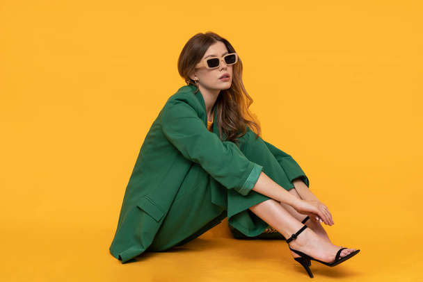 Modna modelka w duym zielonym Fashionable female model in oversized green suit on isolated yellow background. - Photo, image