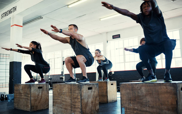 Hold it. a focused group of young people doing lunges on crates as exercise inside of a gym - Фото, зображення