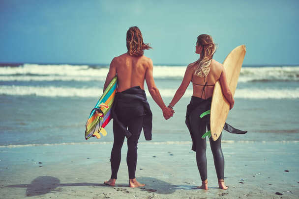 The perfect wave is out there, go find it. Rearview shot of a young couple waiting for the perfect wave - Foto, imagen