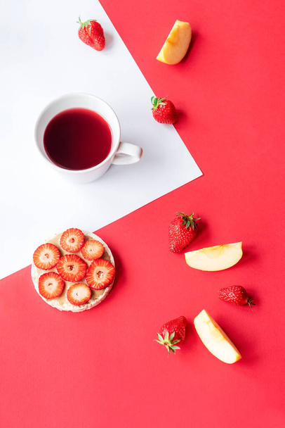 Cup of fruit tea, strawberry sandwich, apple slices on red and white background. Top view. - Photo, Image