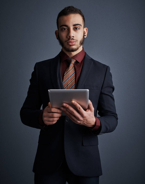 Λίγη τεχνολογία μόνο. Studio πορτρέτο ενός κομψού νεαρού επιχειρηματία χρησιμοποιώντας ένα tablet σε γκρι φόντο - Φωτογραφία, εικόνα