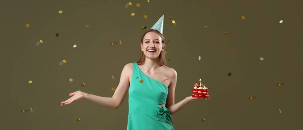 Красивая молодая женщина со сладким тортом день рождения и падения конфетти на цветном фоне - Фото, изображение