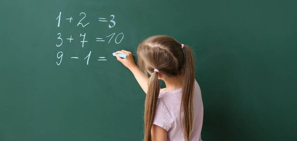 Милая маленькая школьница пишет на доске во время урока математики  - Фото, изображение