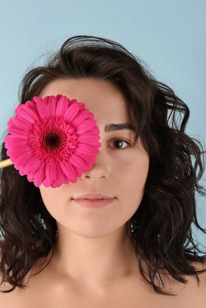 jonge vrouw sluiten oog met mooie gerbera bloem op blauwe achtergrond - Foto, afbeelding