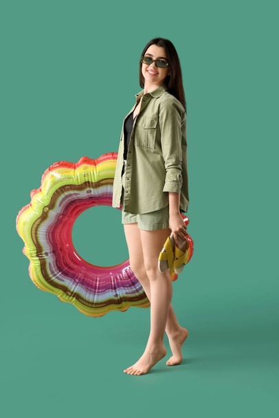 Jonge vrouw met teenslippers en opblaasbare ring op groene achtergrond - Foto, afbeelding